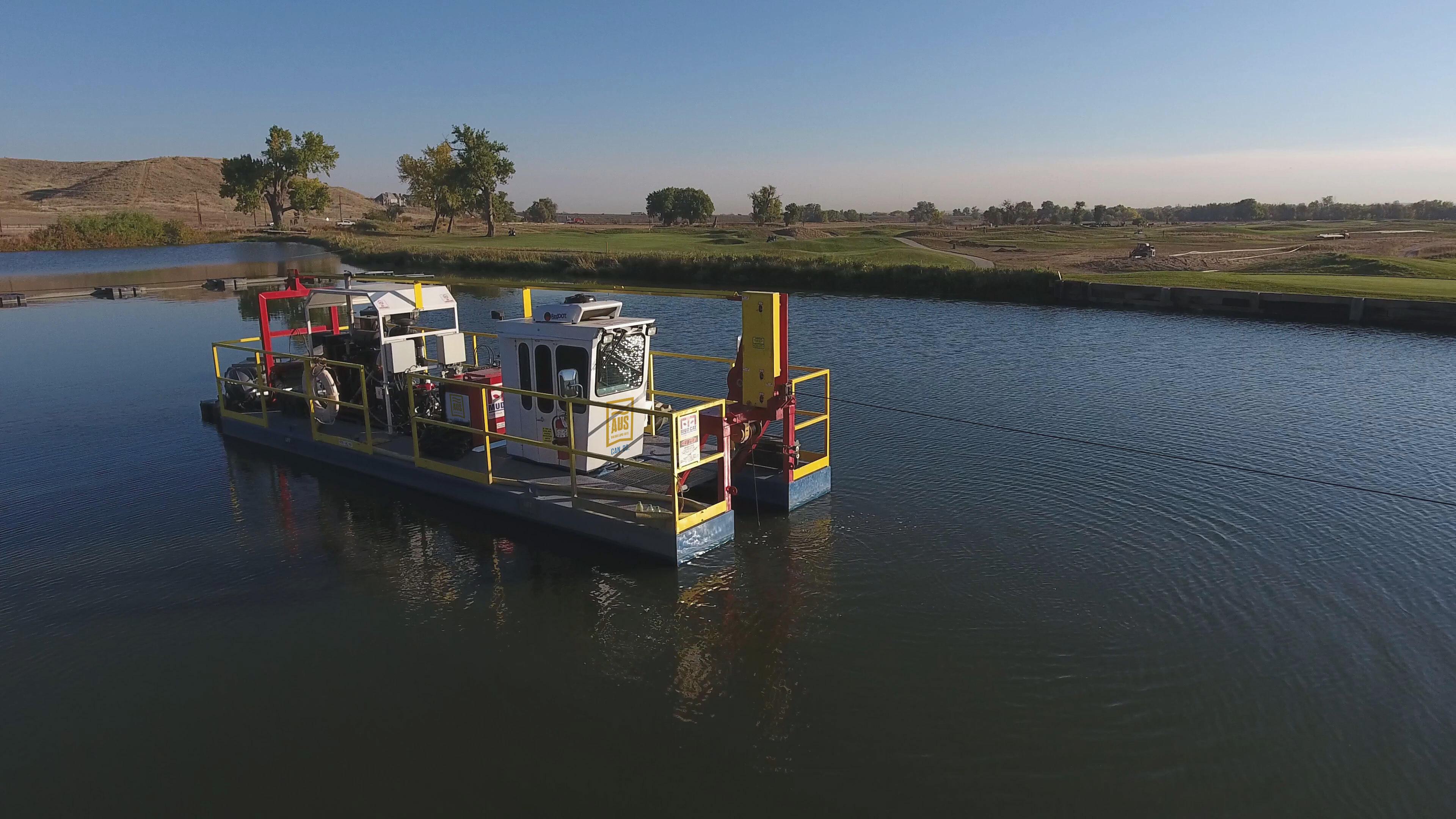 A hydraulic dredger operating in a golf course pond during a sediment removal project, with clear skies and landscaped fairways in the background.