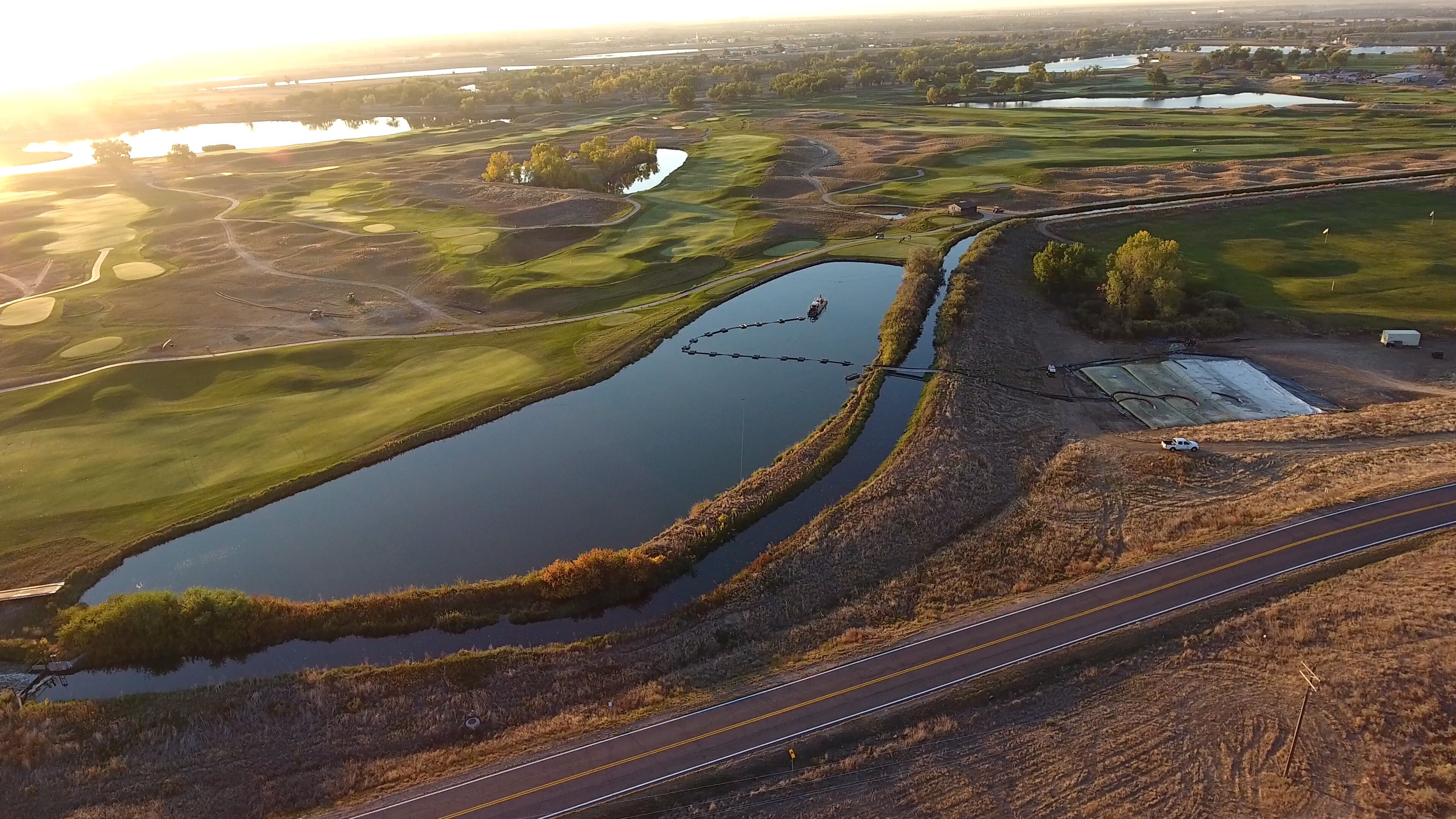 Aerial view of an active golf course dredging project showing a pond with dredging equipment in operation, surrounded by manicured fairways and landscaping during sunset